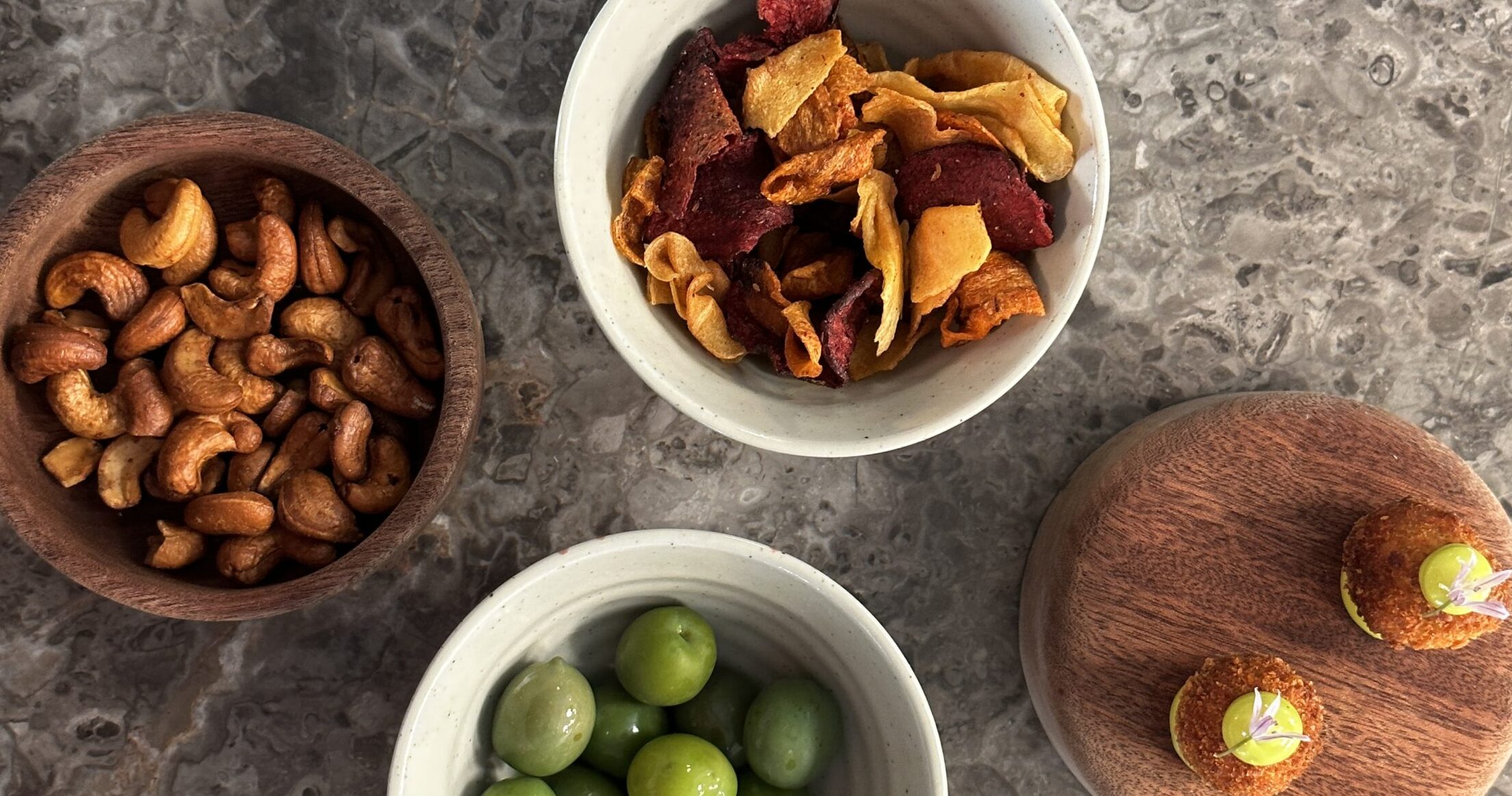 Fire skåle med snacks - soyaristede cashewnødder, rodfrugtechips, oliven og svinekugle